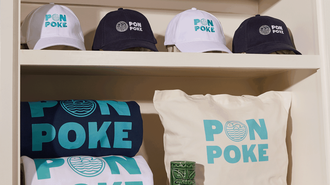 Custom branded hats and t-shirts in blue, white, and black with Pon Poke logo, including a matching pillow – themed merchandise display.