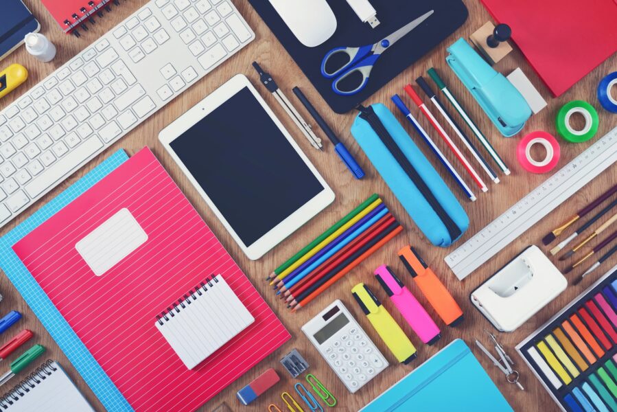 Flat lay of colorful notebooks, pencils, markers, and digital tools on a desk, representing personalized school supplies.
