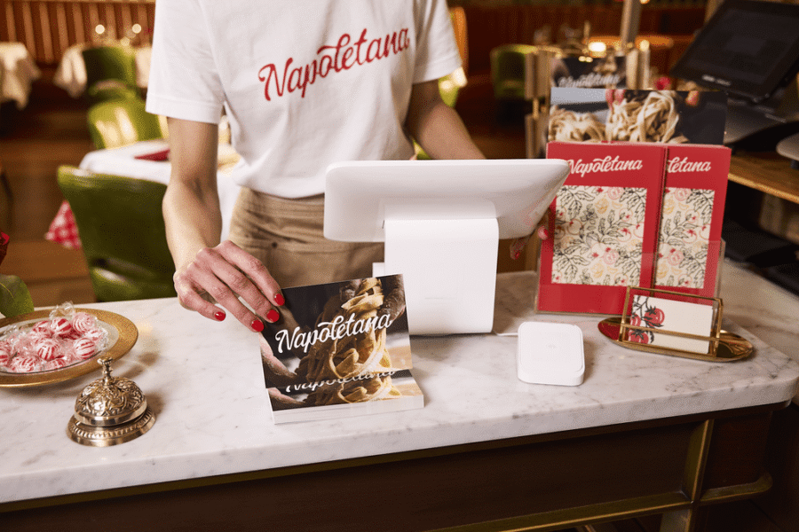 Restaurant host holding a branded postcard at a marble counter, surrounded by menus, business cards and cohesive branding design elements