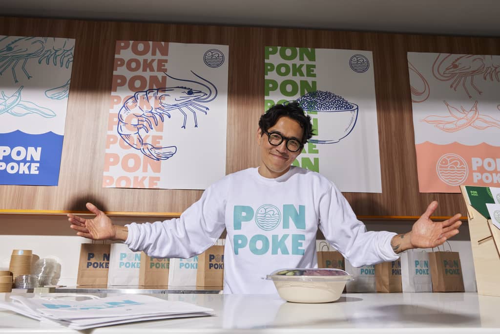 Poke business owner with branded materials including posters and merch