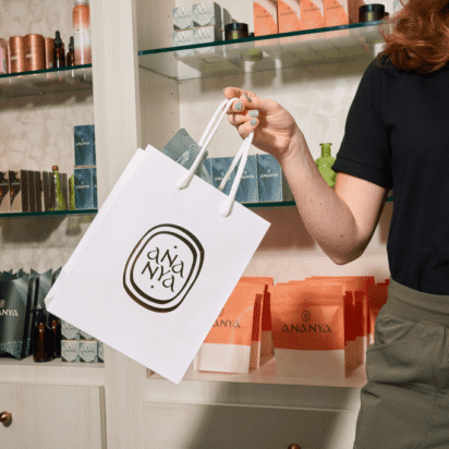 Spa employee holding a branded paper shopping bag with the Ananya logo in a modern retail space
