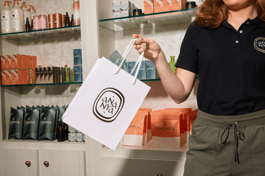 Spa employee holding a branded paper shopping bag with the Ananya logo in a modern retail space