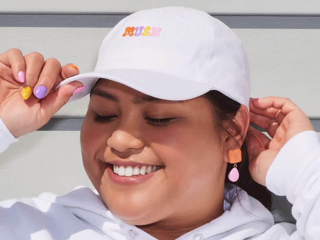 Smiling woman wearing white ball cap with colorful embroidered wordmark logo