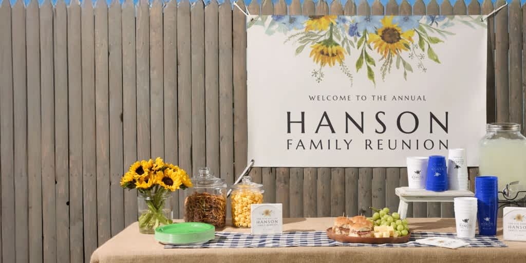 Outdoor event setup with a custom “Hanson Family Reunion” banner featuring sunflower illustrations, displayed above a snack and drink table.