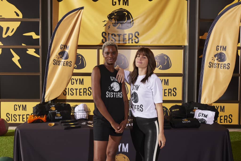 Gym business owners in front of a variety of branded gym signage and merch
