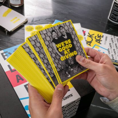 Stack of branded promotional cards with bold yellow design and marketing message held in hands over printed marketing materials