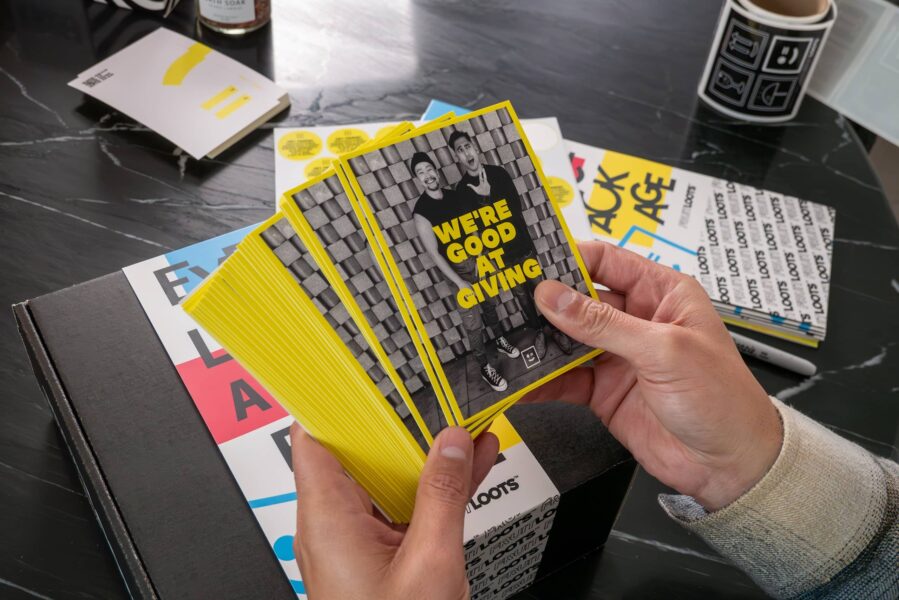 Stack of branded promotional cards with bold yellow design and marketing message held in hands over printed marketing materials