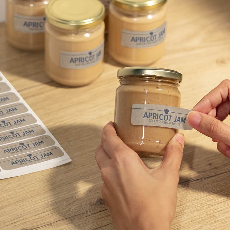 A person applying branded sustainable stickers made from eco-friendly sticker materials to a jar