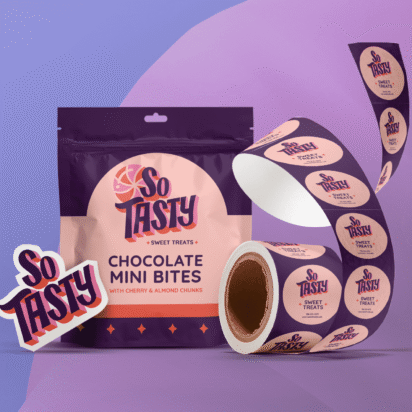 A colourful package of "So Tasty" chocolate mini bites is featured with a background of its brand colours - indigo, purple and a peach pink. The image also features a roll of similarly branded circle stickers, demonstrating VistaPrint product offering.