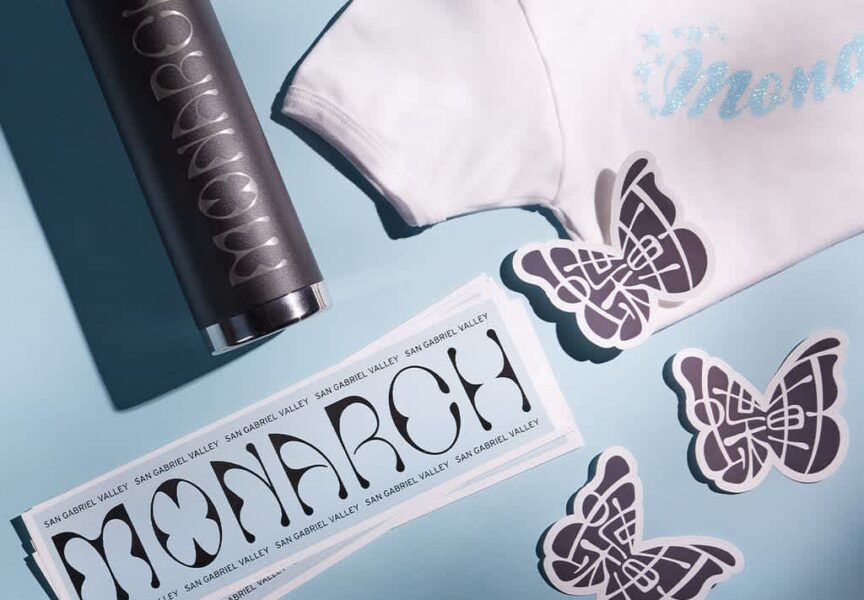 Sample set of Monarch-branded giveaways including a water flask, T-shirt, bumper sticker, and mini stickers of brand&rsquo;s butterfly mark.