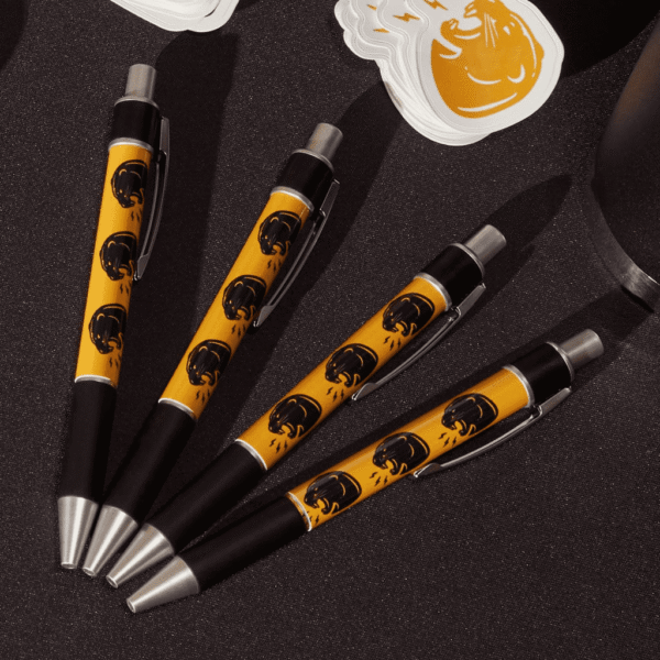 Custom pens feature roaring panther heads on a yellow body, laying on a booth table in fan shape.