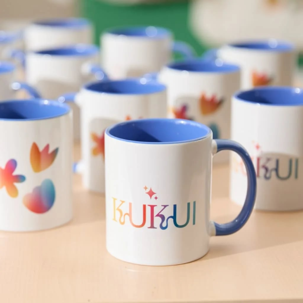 Example of &ldquo;Kukui&rdquo; branded mug features rainbow gradient branding, floral shapes and colored handle that matches inside of mug.