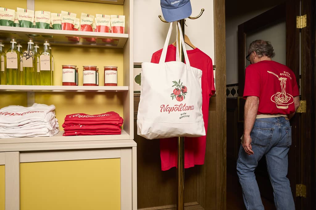Shelves displaying branded merch for an Italian restaurant including a tote bag with an illustration of tomatoes