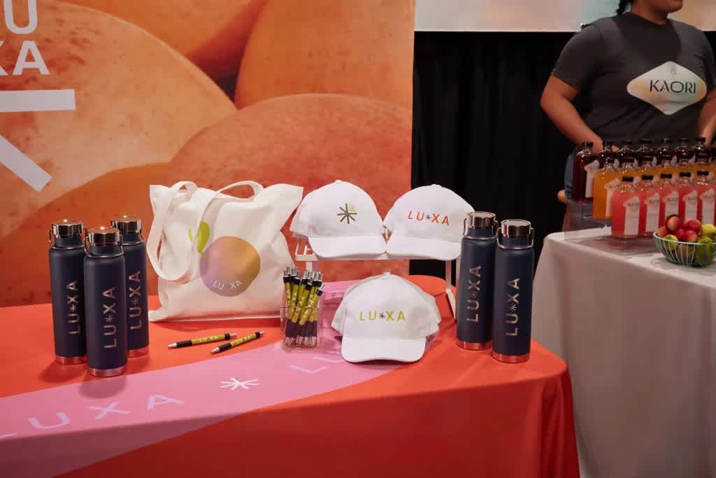A trade show booth with a selection of branded promotional items: water bottles, caps, pens, tote bags
