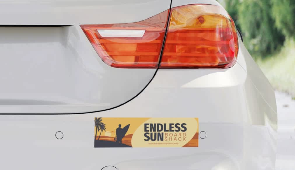 A white car with a branded sticker for a surf shop on the bumper