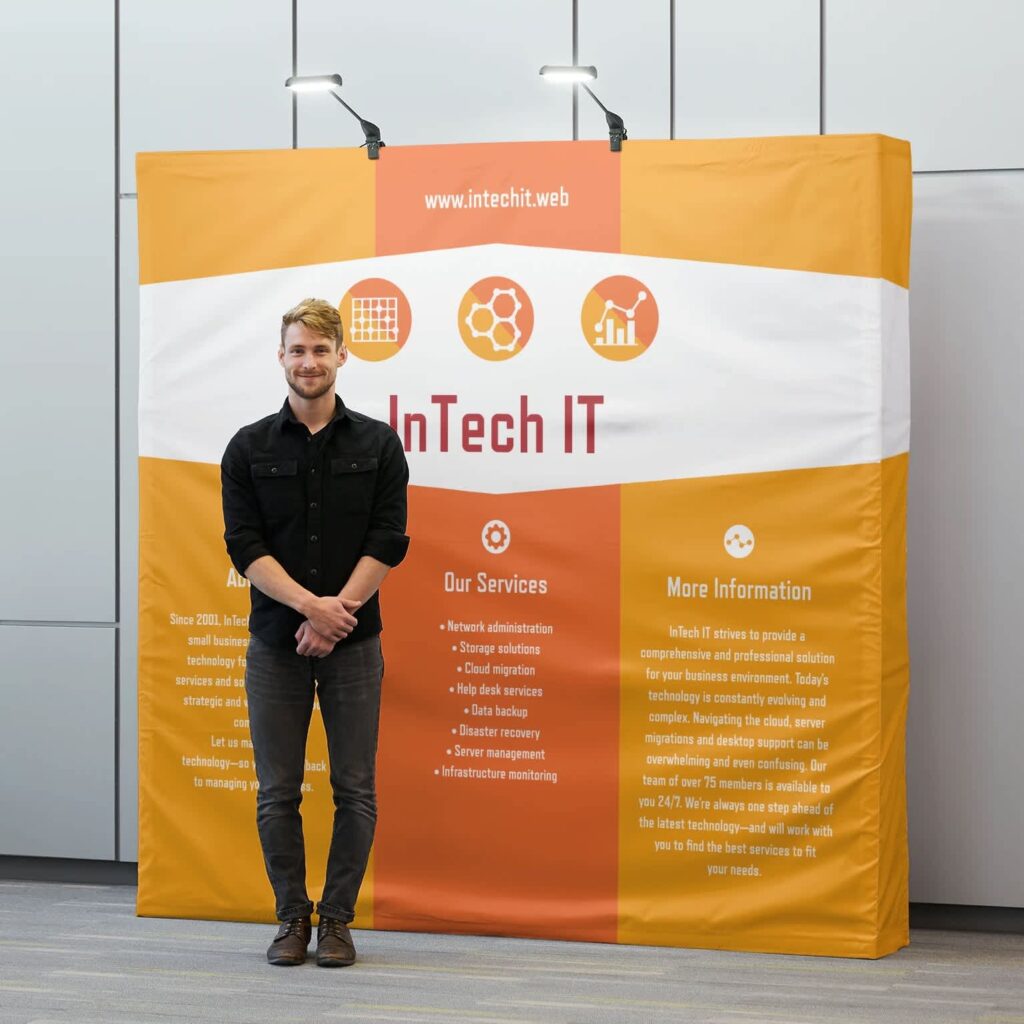 A person standing in front of a branded InTech IT banner featuring the business overview and the list of services they offer