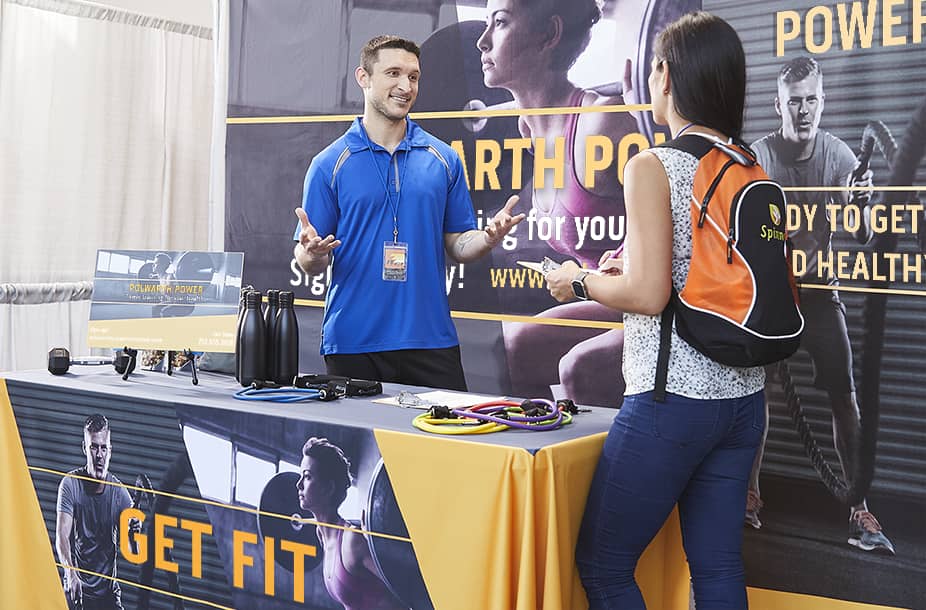 A man and woman talking at a branded booth for a gym at an event