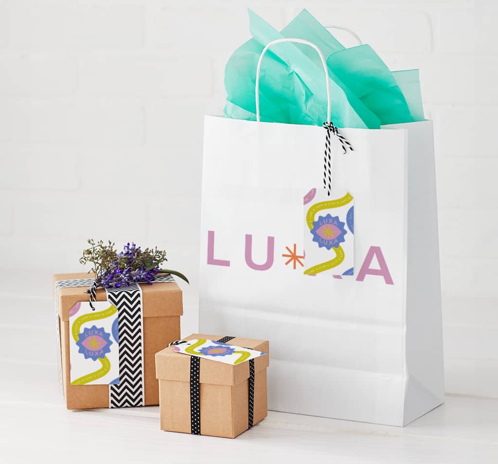 Branded white paper shopping bag with turquoise tissue and two small cardboard boxes wrapped in ribbon
