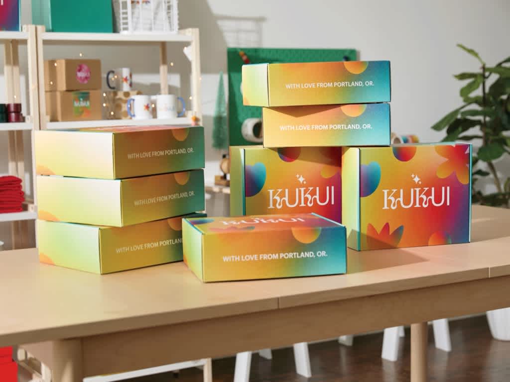 A desk with a stack of brightly colored branded cardboard box designs with a white brand logo.