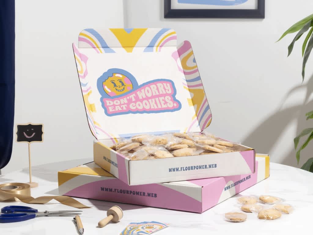 A cardboard box with cookies inside, sat open on a table showing bold branding with a slogan and smiley face design.