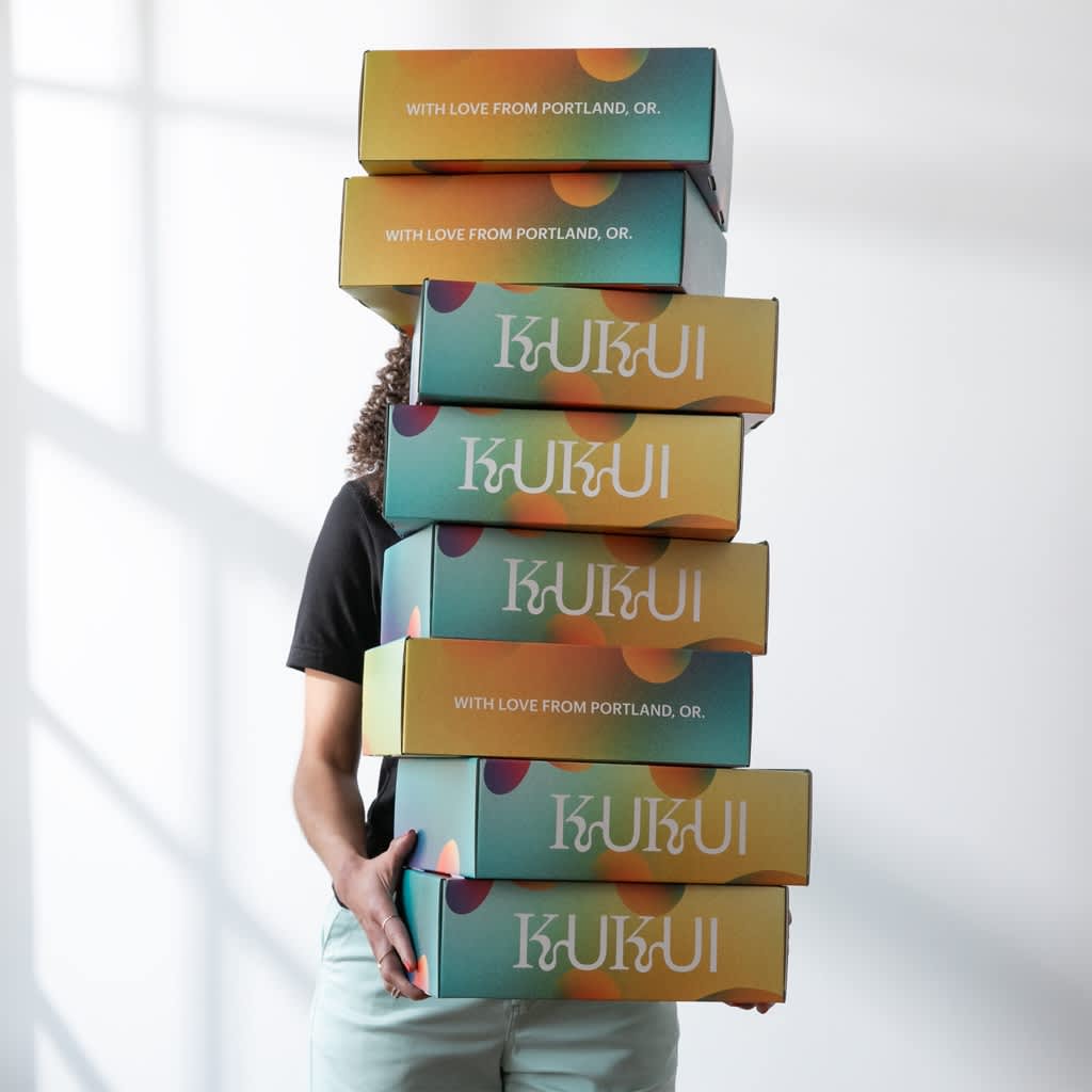 A person holding a tall stack of multicolored branded cardboard boxes.