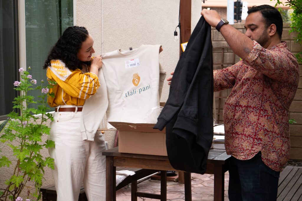 Two people unboxing a package and pulling out branded sweaters