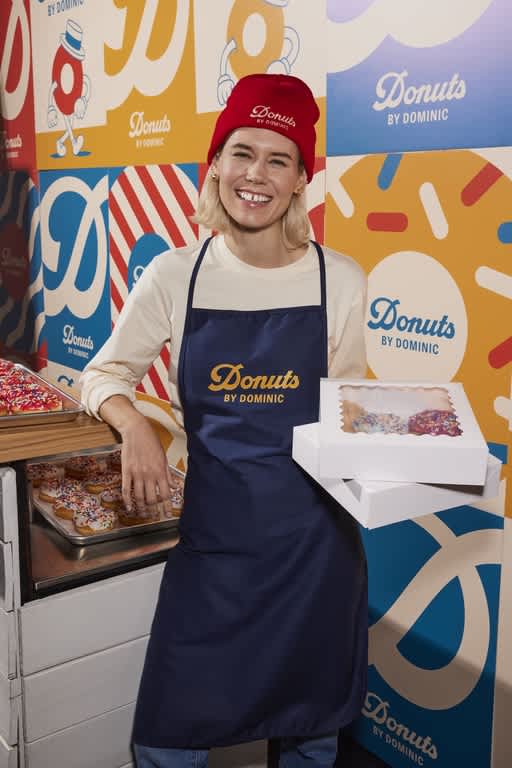 Small business owner wearing branded merch holding box of donuts.