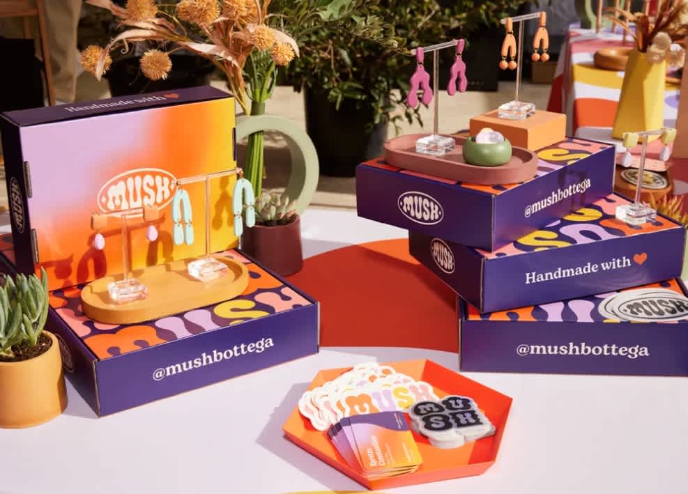 A display of handmade jewellery products by brand Mush on top of brightly colored branded boxes.