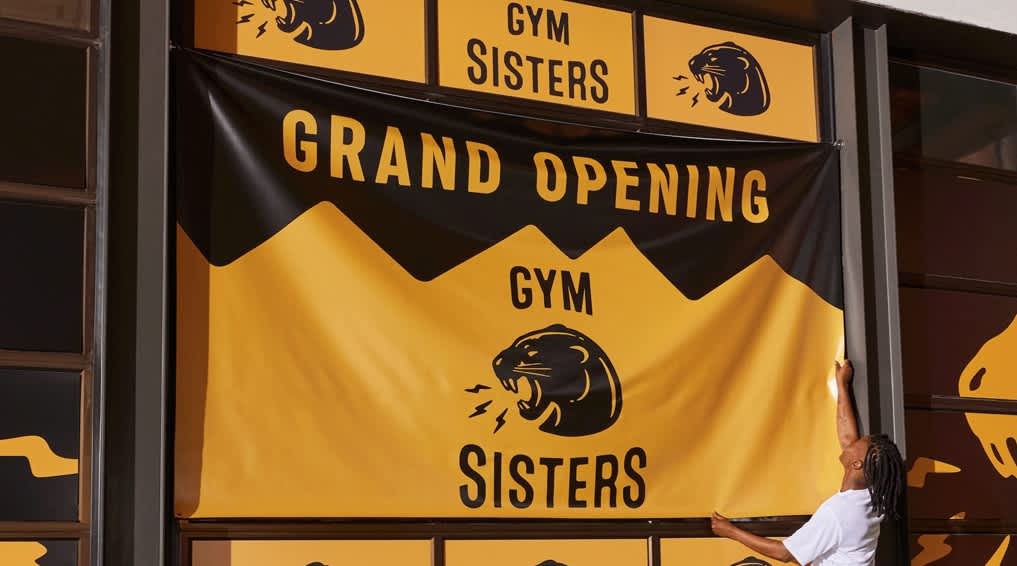 Business owner hanging large black and yellow banners promoting grand opening of a gym.