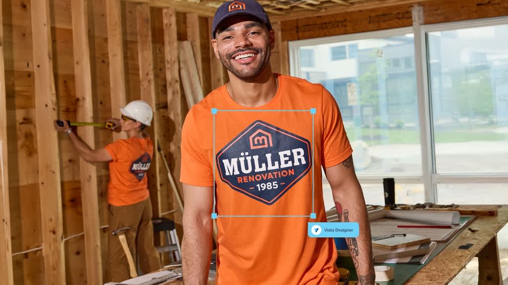 Two construction workers on building site wearing bright orange T-shirts with large centrally placed logo on front and back that reads “Muller Renovation 1985”