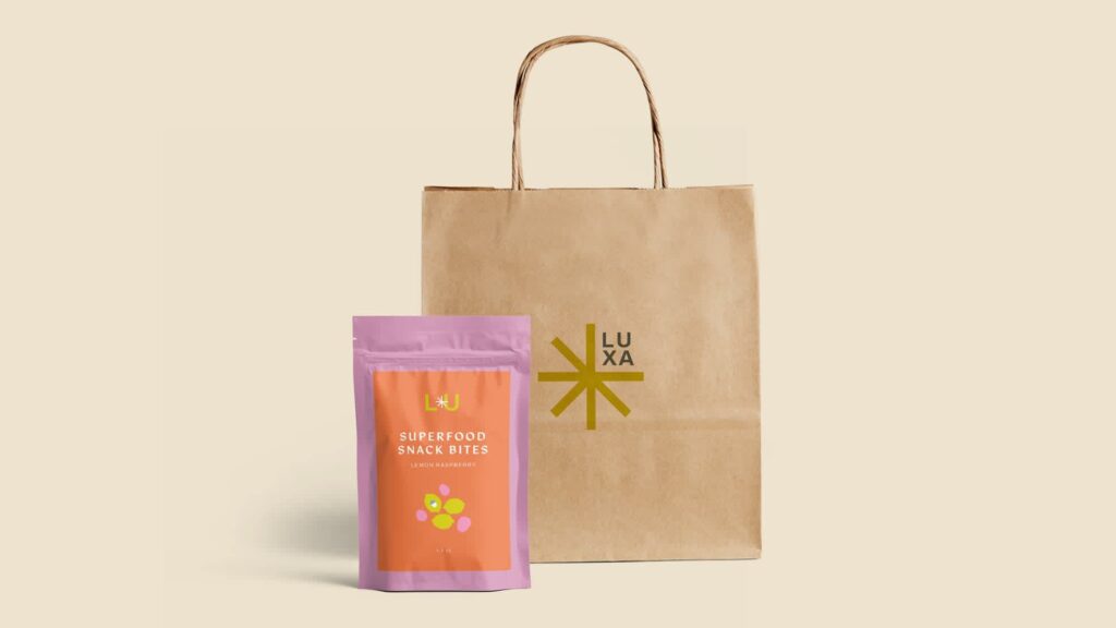 Brown paper bag with simple &ldquo;Luxa&rdquo; logo and pink and orange sealable pouch featuring &ldquo;superfood snack bites&rdquo;.