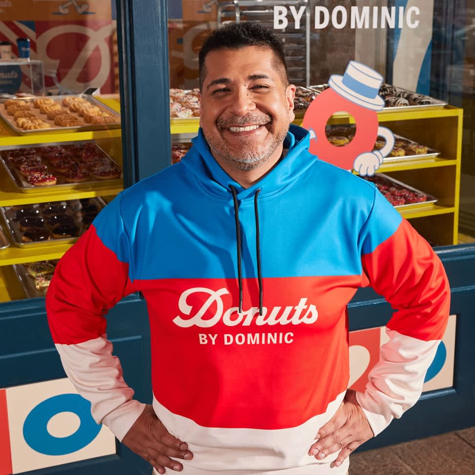 A donut store employee wearing a branded hoodie in brand colors with the brand logo.