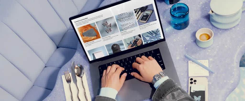 POV image of hands typing on a laptop scrolling through fashion website at restaurant table.