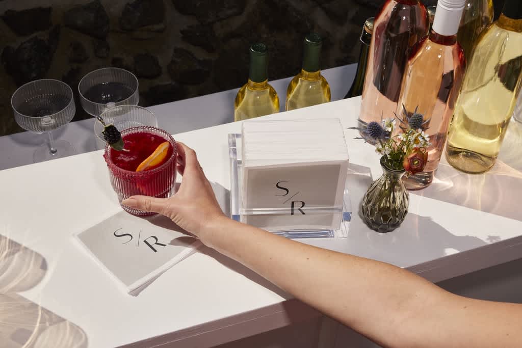 Hand holding a red drink on a white table surrounded by branded wedding stationery.