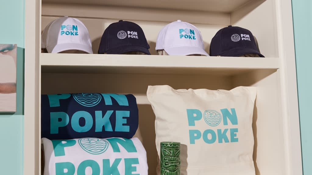 A shelf featuring white and blue branded merchandise for a poke restaurant with a bold logo.