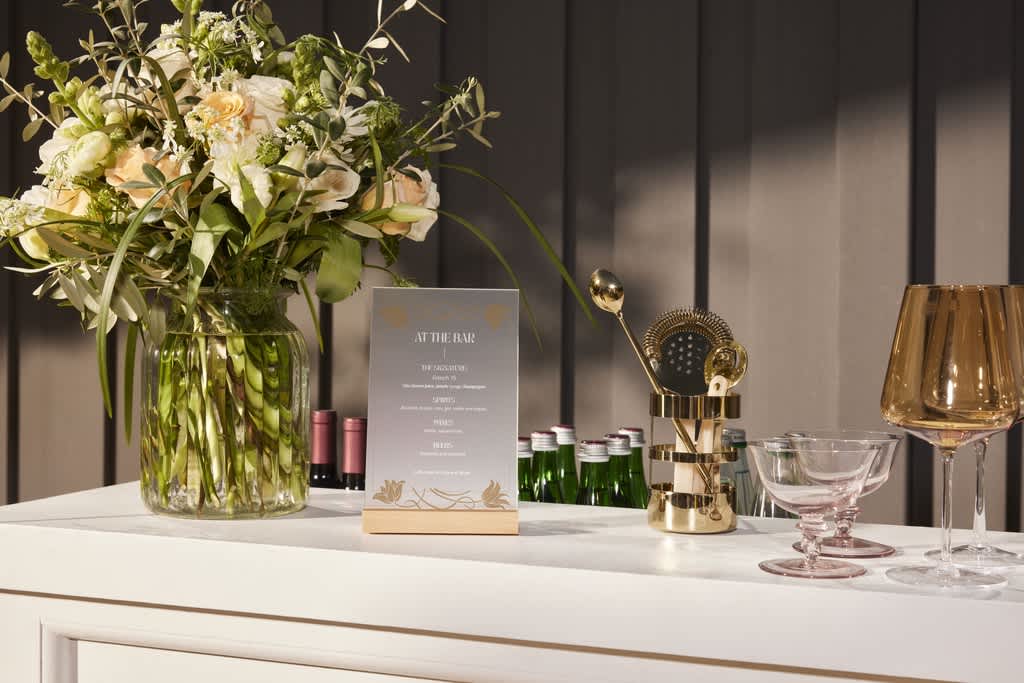 A wedding bar with a vase of flowers, cocktail glasses and a shaker with cocktail making equipment.