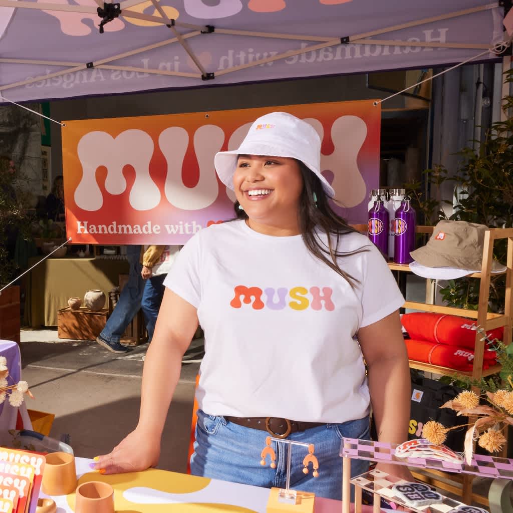 A woman wearing a white branded T-shirt and hat in front of a banner with a playful logo.