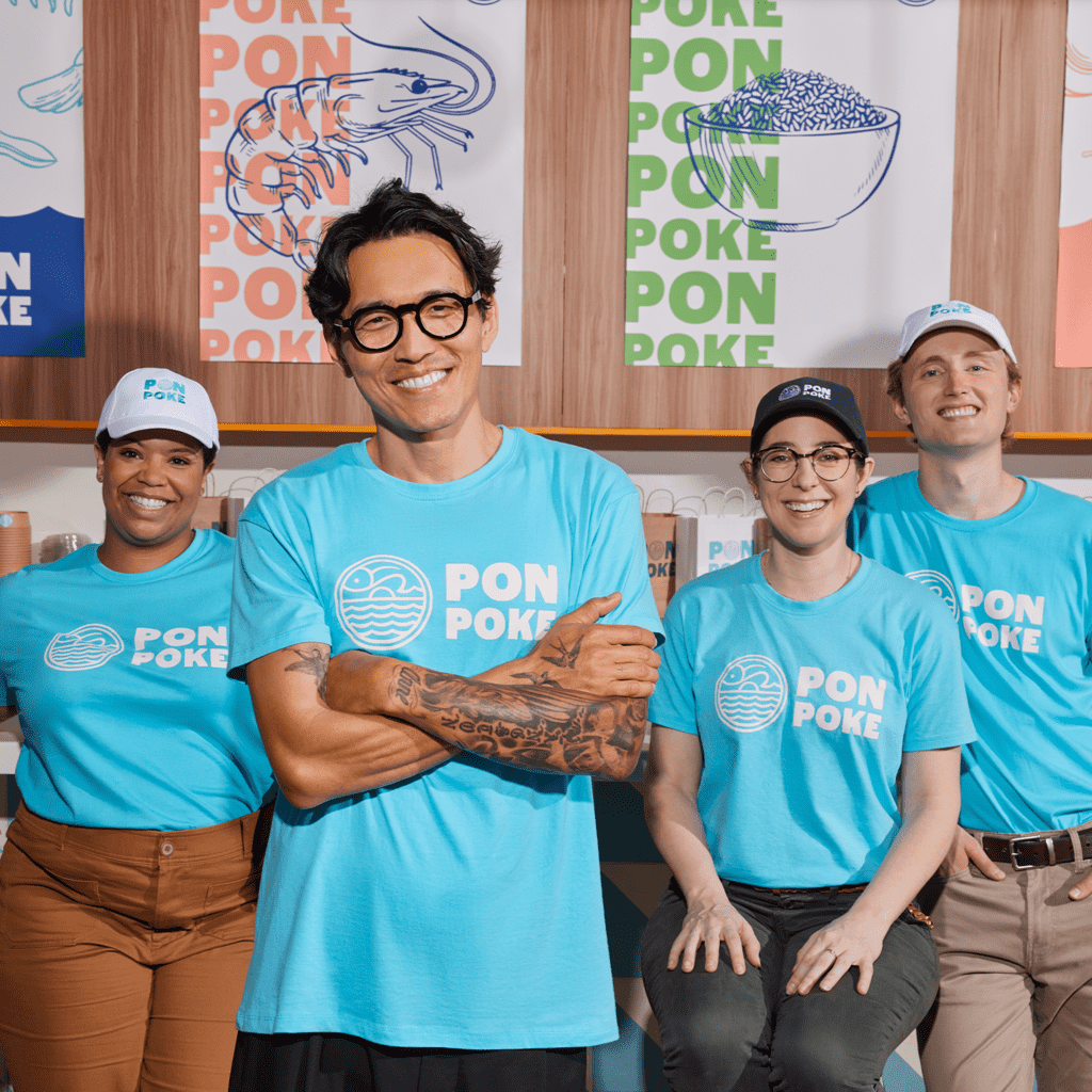 Four team members in a poke shop wearing identical light blue T-shirts with white circular logo and font &ldquo;PON POKE.&rdquo;