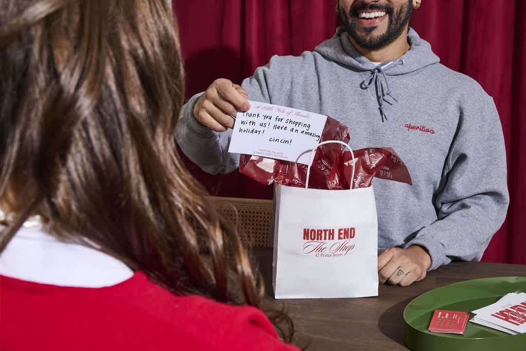 Staff member handing a branded holiday bag and card to a customer in a festive shop setting.