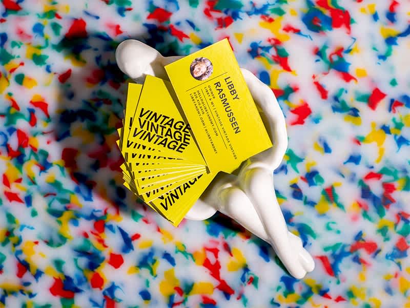 Fanned out selection of yellow business cards with black font in a ceramic bowl on a terrazzo counter for a vintage store owner.