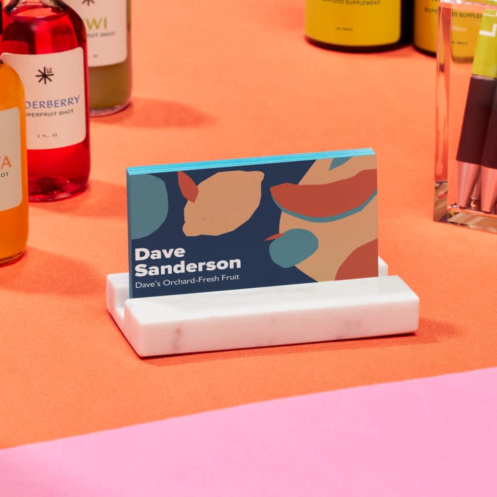 Dark blue business card with orange and blue fruit shapes, chunky white font for business owner name and light blue painted edges.