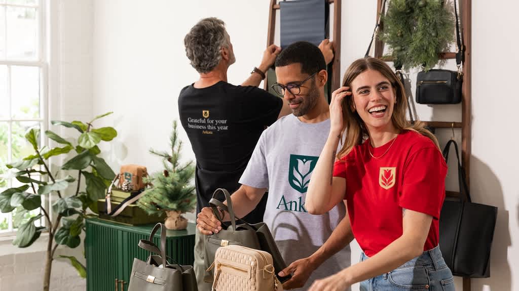 Three members of a team in a shop. One in a red T-shirt with a small yellow flower logo; One in light gray T-shirt with a large dark green flower logo; And one wearing black T-shirt with white font &ldquo;grateful for your business this year.&rdquo;