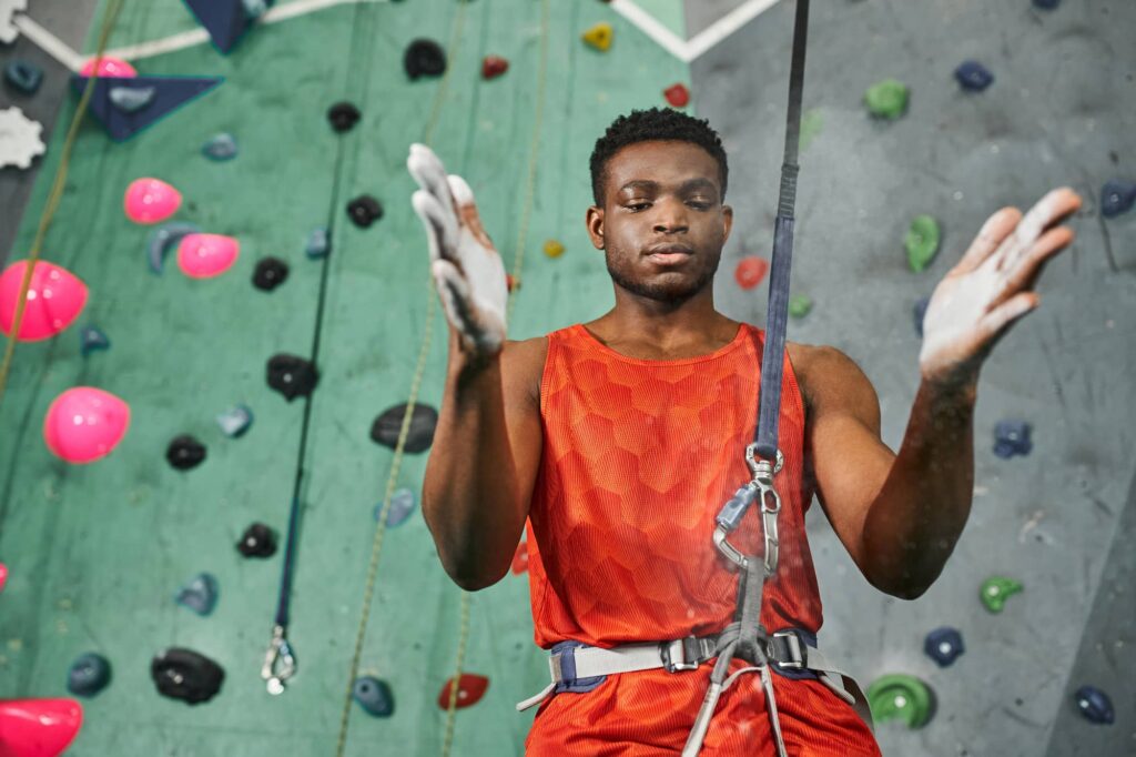Person wearing an orange athletic sleeveless shirt while preparing to climb on an indoor climbing wall.