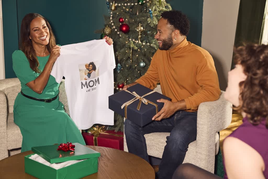 Woman holding up custom shirt gift that reads “Mom” with a picture of her child.