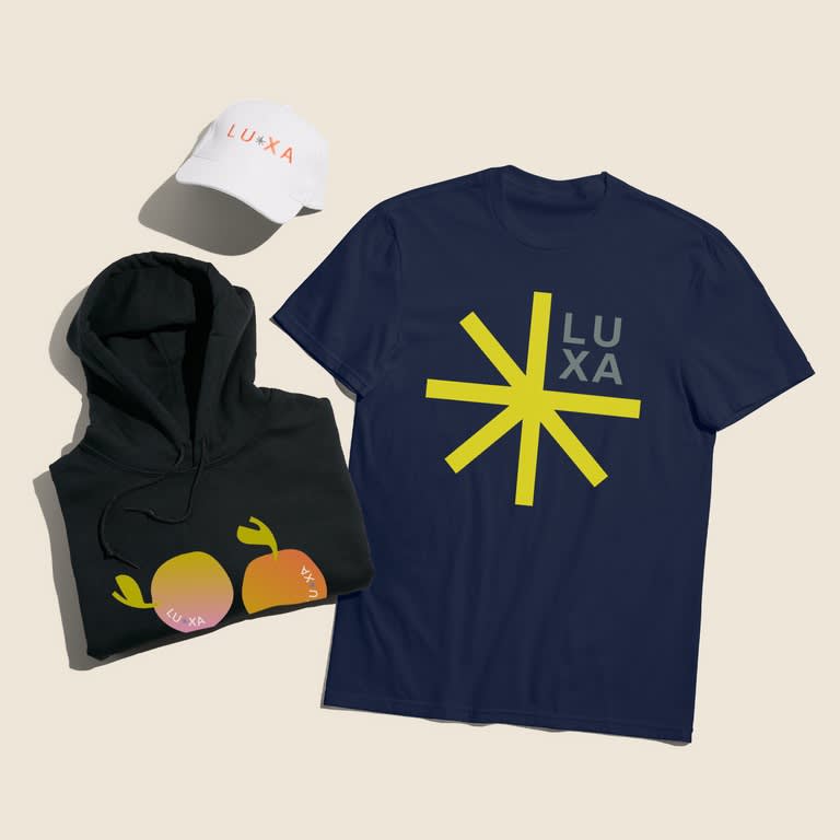 Flat lay of a navy T-shirt, black hoodie and white cap with matching branded graphics.