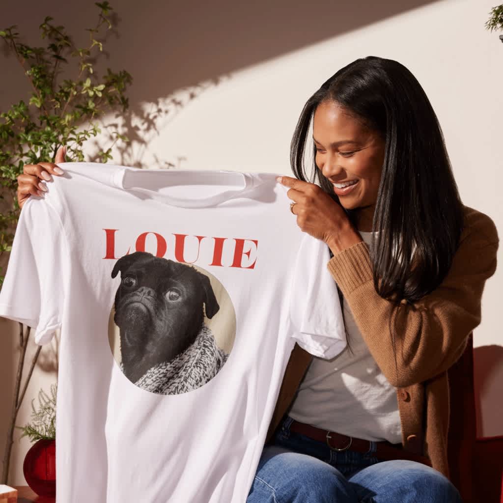 Person holding a custom T-shirt printed with a pet pug photo and logo design.
