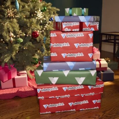 Stack of wrapped gift boxes beside a decorated Christmas tree in a cozy room.