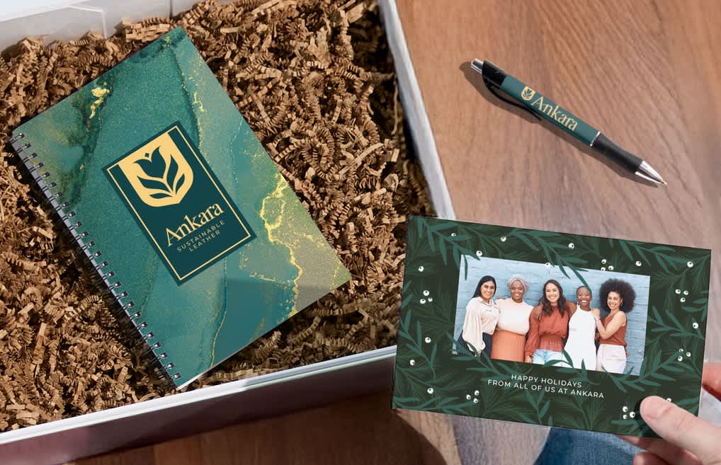 Open gift package holding a branded notebook with kraft paper filling and a holiday greeting card.