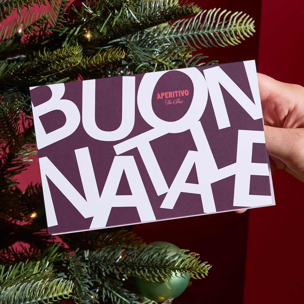 Matte Christmas postcard with bold typographic design and subtle brand logo held in front of a decorated Christmas tree.