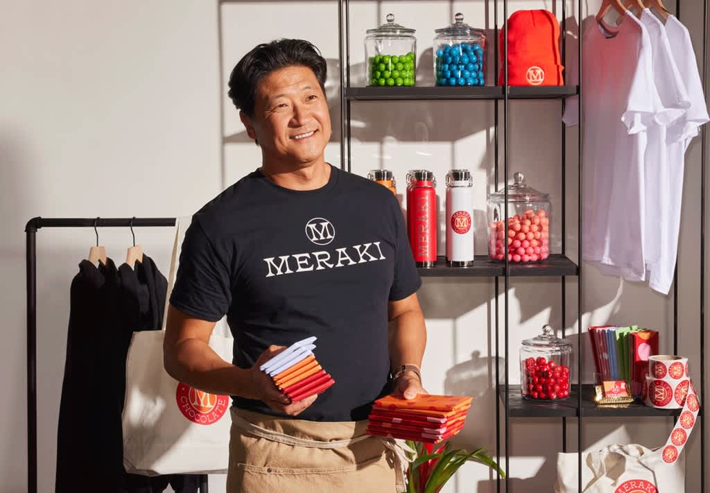 Person wearing a branded black T-shirt while holding folded fabric samples in a merch display area.